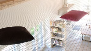 A high-ceilinged room with a wooden beam structure, a netted window, and a small bookshelf with books. - casa Rosa milo (Milo)