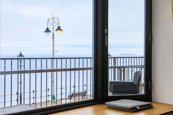 Une chambre avec vue sur la mer, un balcon avec un fauteuil et une table avec un ordinateur portable.