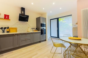 Uma cozinha moderna com armários cinza, uma coifa preta e um espaço de refeições com uma mesa redonda e cadeiras amarelas.