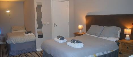 A hotel room with a large bed, a smaller bed, two bedside tables with lamps, a door, and a striped carpet.