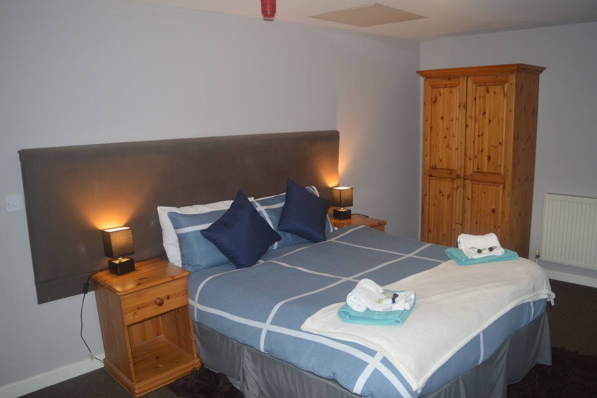 A bedroom with a large bed, two bedside tables with lamps, a wooden wardrobe, and a radiator.