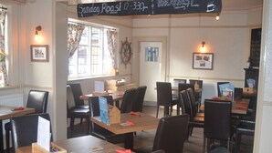 A restaurant with wooden tables and black chairs, a chalkboard menu, and framed pictures on the walls. - The Queen Victoria (King's Lynn)