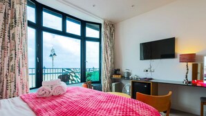A hotel room with a bed, a desk, a TV, and a balcony with a view.