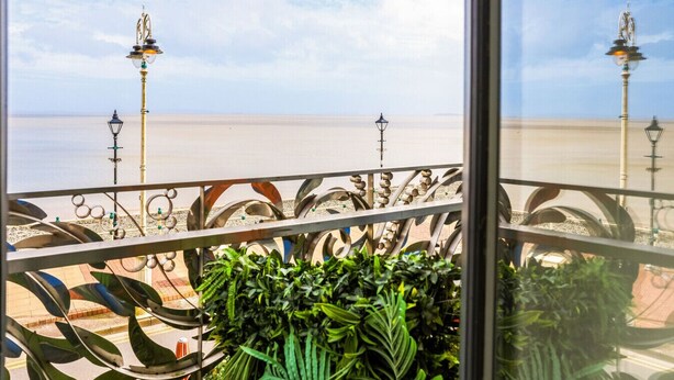 A balcony with a view of the beach, metal railings, and street lamps.