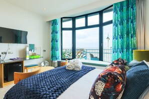 Ein Hotelzimmer mit Bett, Schreibtisch, Fernseher und einem Balkon mit Vorhängen.