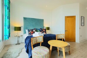 Ein Schlafzimmer mit einem Bett, zwei Stühlen, einem kleinen Tisch, einer Holztür und einem Fenster mit Vorhängen.