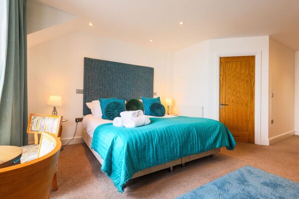 A bedroom with a bed, bedside lamps, a wooden door, and a blue rug.