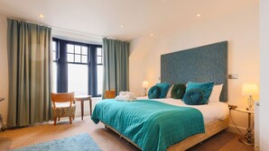 A hotel room with a bed, two chairs, a desk, a window, and a wall-mounted lamp. - Coastal Elegance - Seaview Double Room (Vale of Glamorgan)