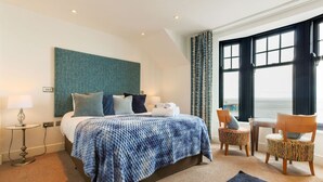 Habitación de hotel con cama, una mesita, una silla y vista al mar.