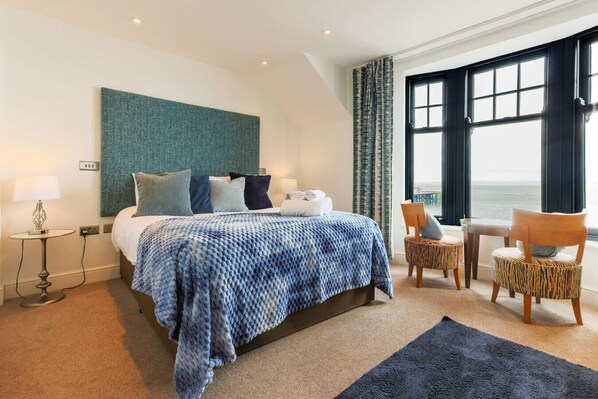 A hotel room with a bed, a small table, a chair, and a view of the sea. - Coastal Bliss at its Finest - Seaview Double Room (Vale of Glamorgan)