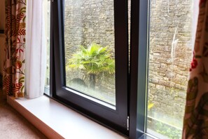 A window with a view of a stone wall and a small plant. - Double Room Courtyard Penarth (Vale of Glamorgan)