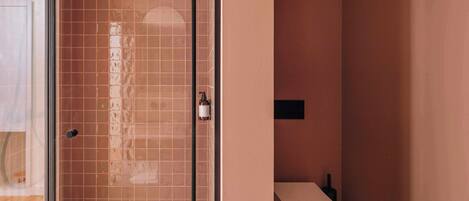 A bathroom with a glass-enclosed shower, a toilet, and a small shelf with a bottle.