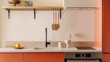 Eine Küche mit einer Holzschüssel voller Orangen auf einem Regal, einer Topfhalterung, einem Spülbecken, einem Herd und einem Schrank.