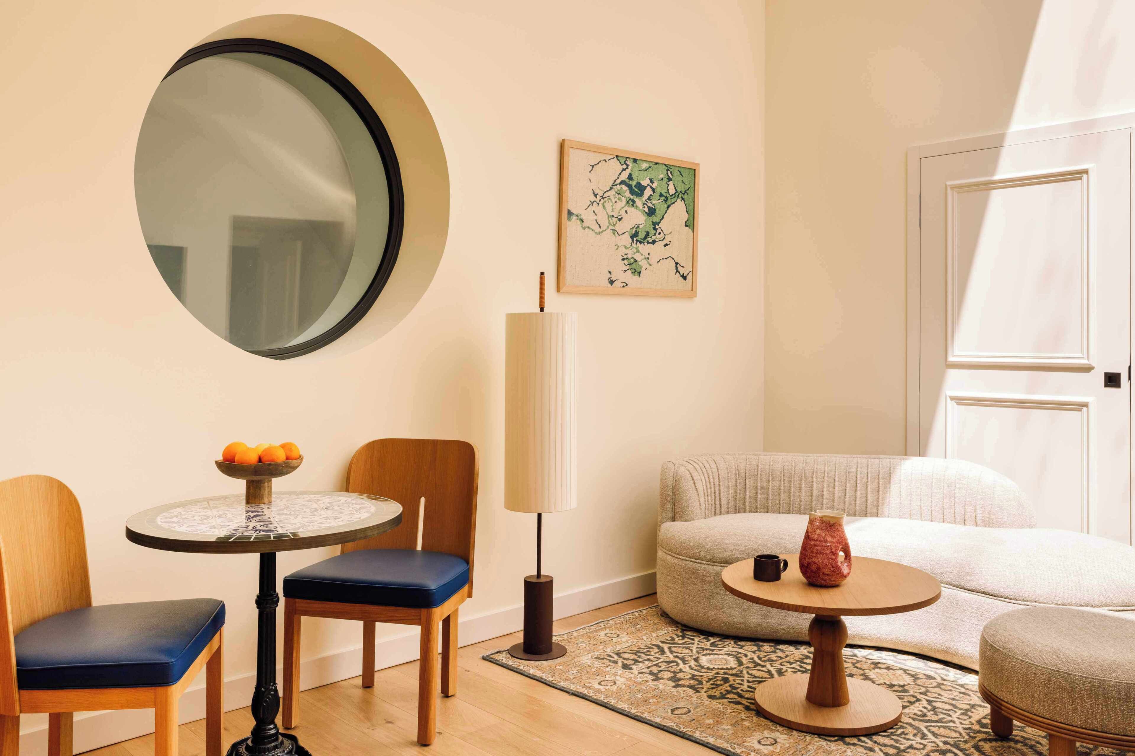Un salon moderne avec une table ronde, deux chaises, un canapé, une petite table ronde ornée d’un vase, une lampe et un grand miroir accroché au mur.
