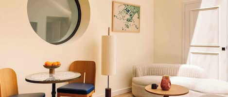 Una sala moderna con una mesa redonda, dos sillas, un sofá, una pequeña mesa redonda con un jarrón, una lámpara y un espejo grande en la pared.