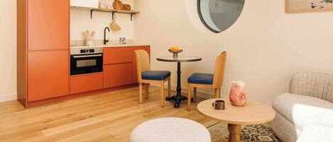 Un espacio habitable compacto con kitchenette, una mesa de comedor redonda, dos sillas, un reposapiés redondo y un sofá.