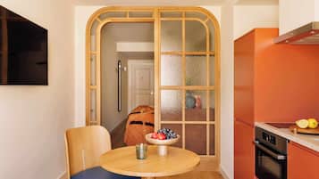 A compact kitchen with a round table, a chair, and a bowl of fruit.
