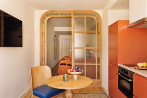 Una cocina compacta con una mesa redonda, una silla azul y un cuenco de fruta.