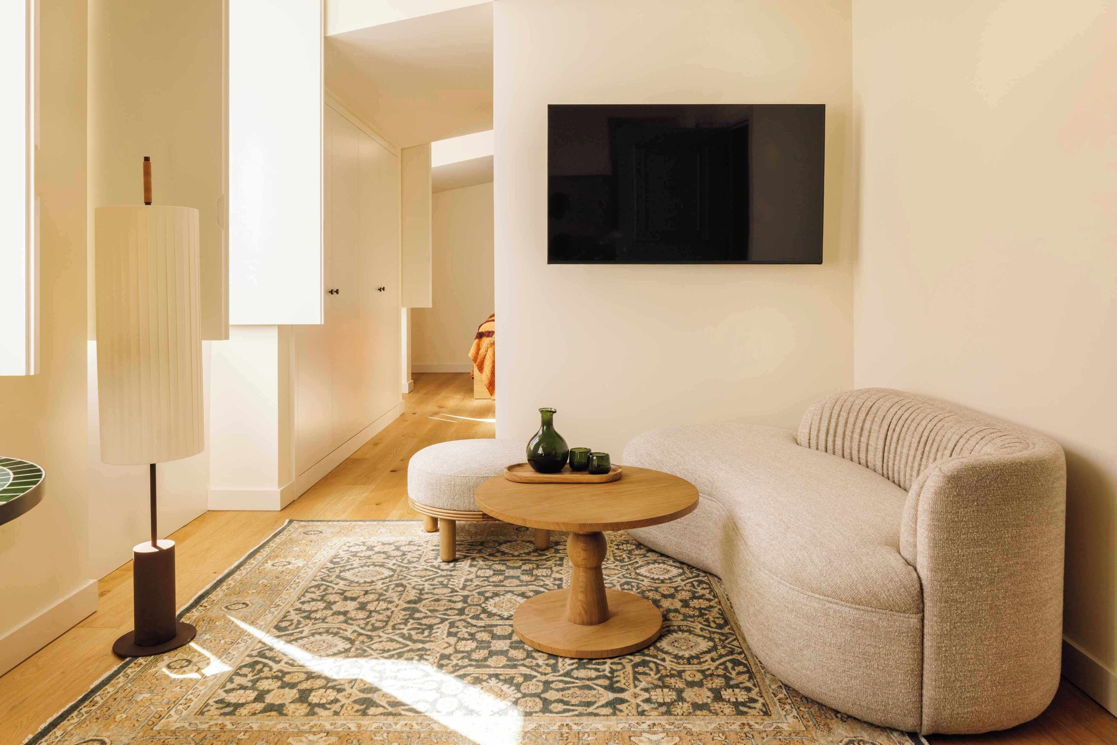 A modern living room with a beige sofa, a round wooden coffee table, a patterned rug, and a floor lamp.