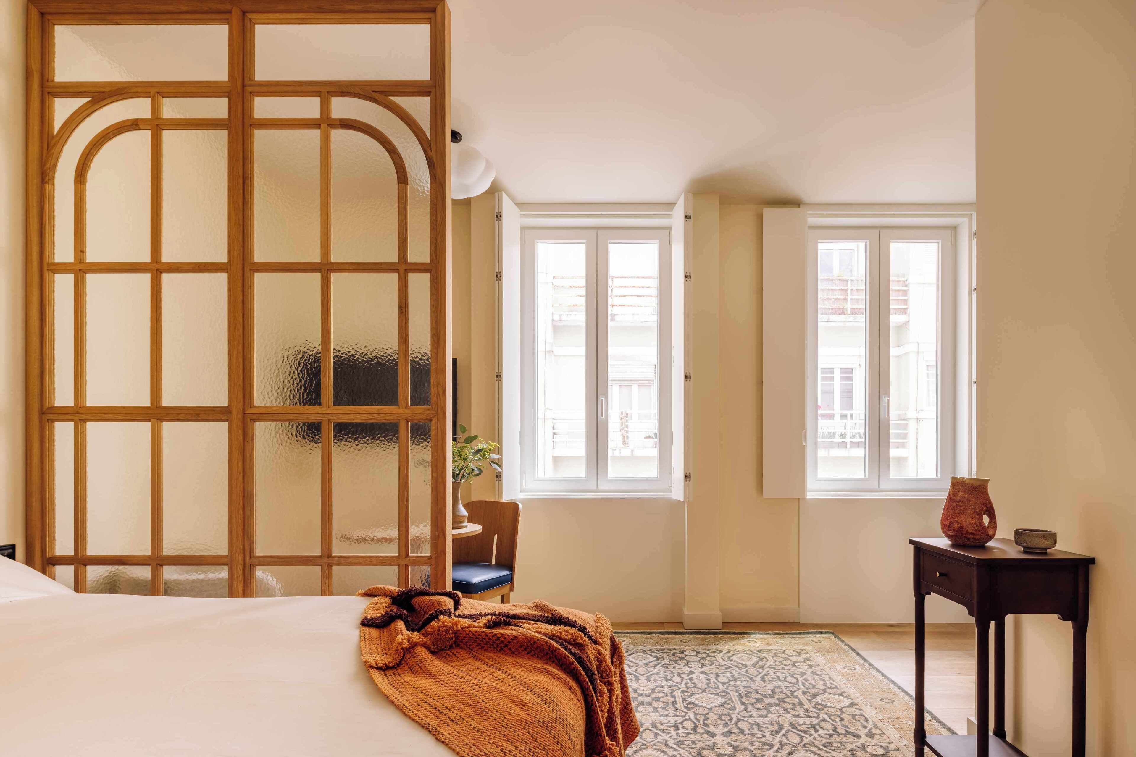 A bedroom with a bed, a wooden screen, a chair, a small table, and a window.