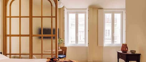 A bedroom with a bed, a wooden screen, a chair, a small table, and a window.