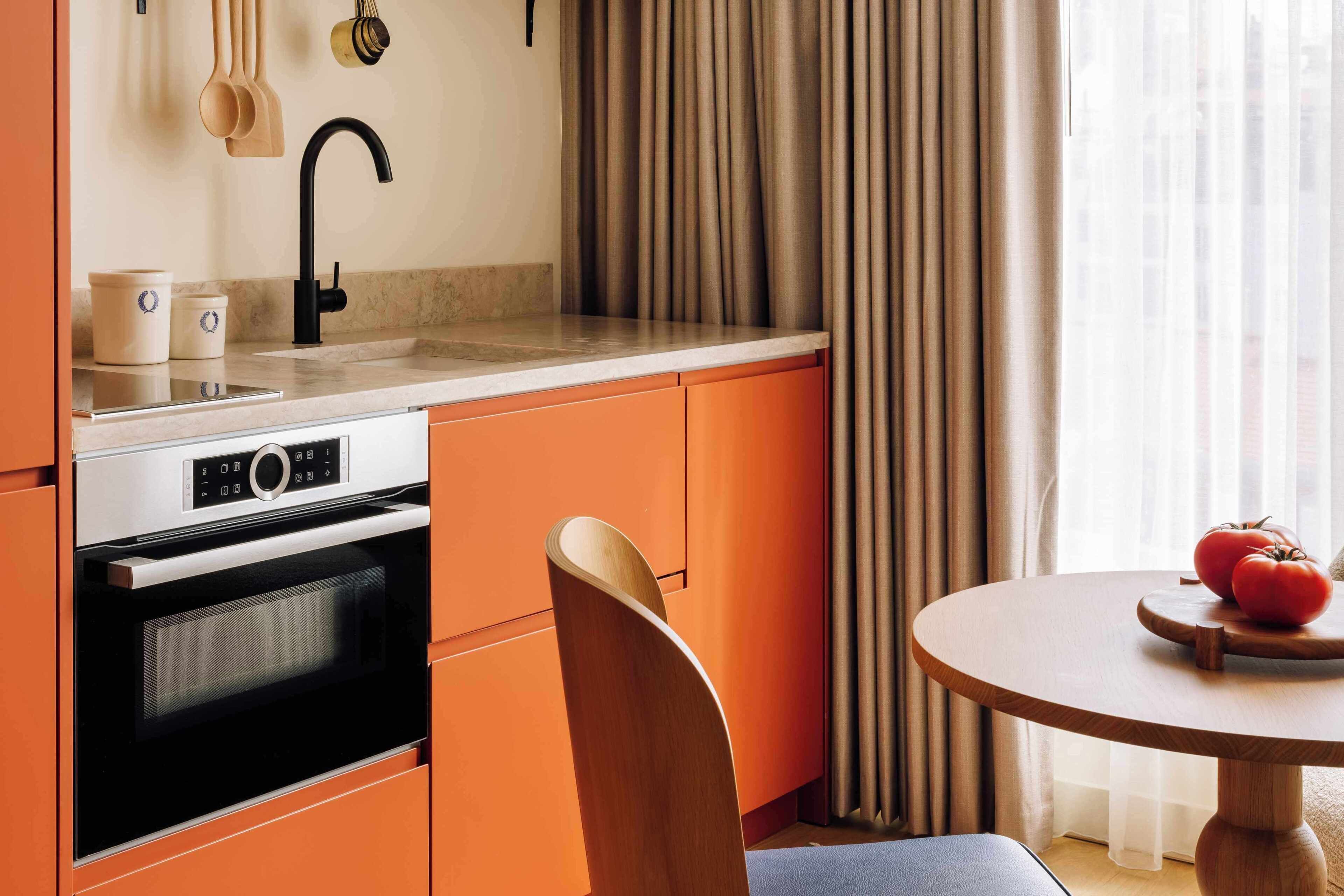 Eine Küche mit orangefarbenen Schränken, einem schwarzen Wasserhahn, einer Mikrowelle und einem Tisch mit Holzfuß.