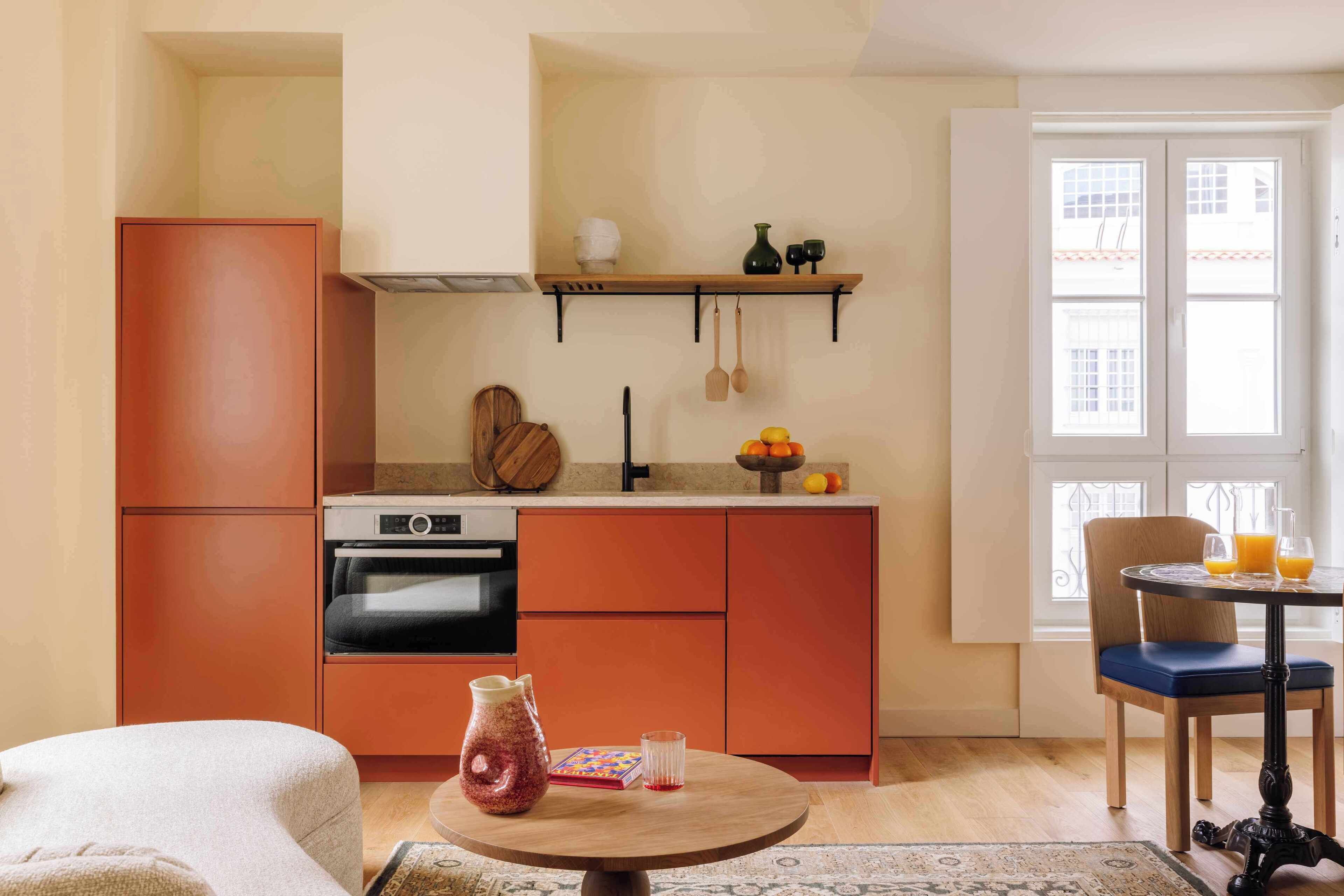 A compact kitchen with a built-in oven, a dining area with a round table, and a window with a view of the outside.