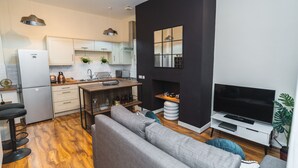 A modern kitchen with white cabinets, a built-in oven, and a dining area with a wooden table and bar stools. - Dale Street - Modern City Centre Apartment (Liverpool)