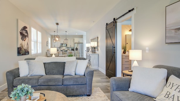 A modern living room with a grey sofa, a coffee table, and a kitchen in the background.