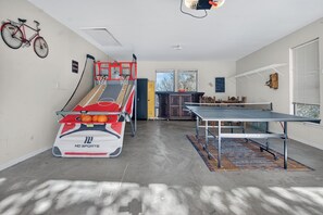 Una cancha de baloncesto con un aro rojo y blanco, una mesa de ping pong y una bicicleta colgada en la pared.