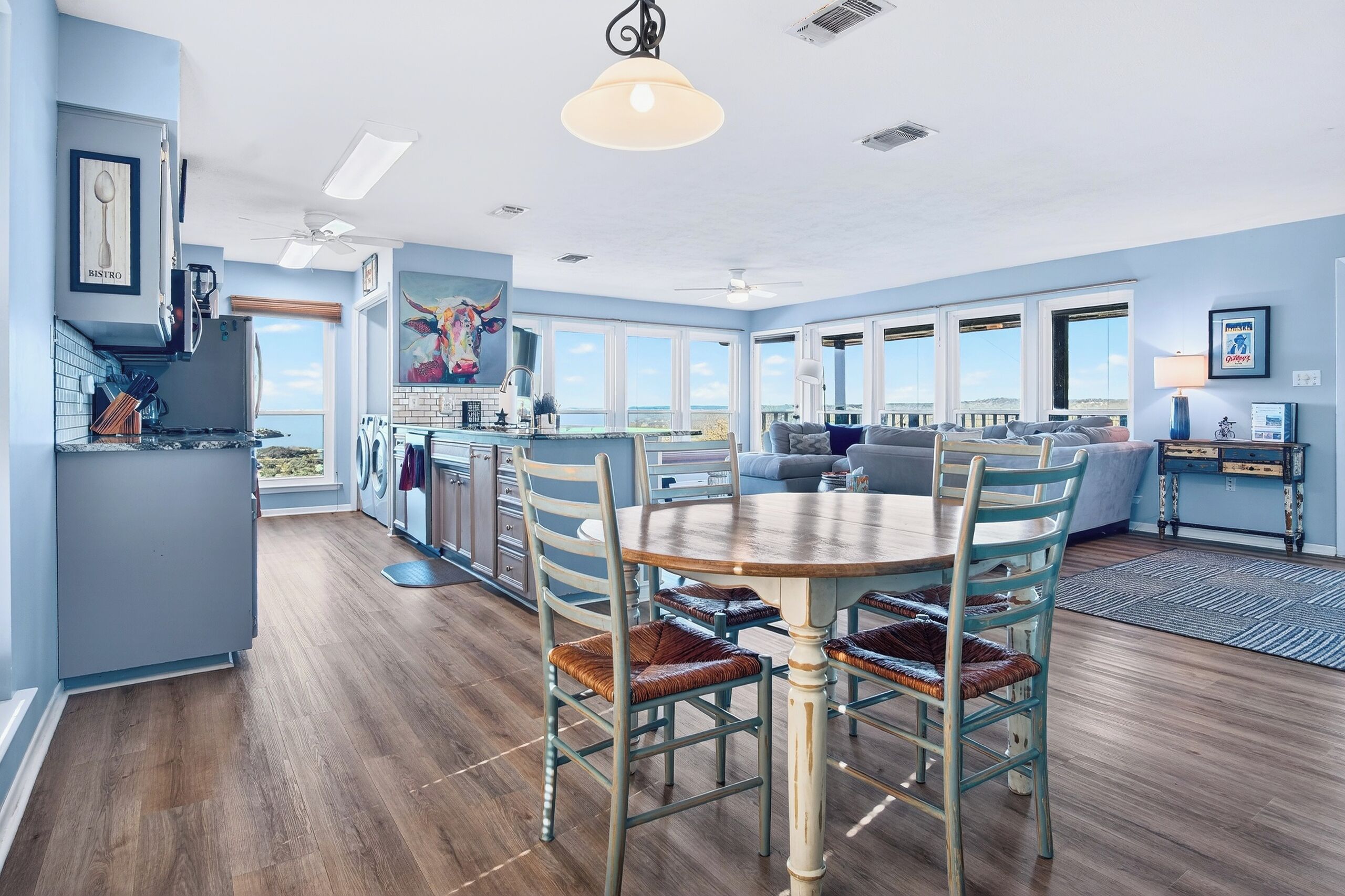 Un vaste espace de vie comprenant un coin repas avec table et chaises, une cuisine dotée d’une grande fenêtre et une vue sur l’océan.