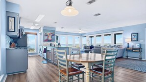 A spacious living area with a dining table and chairs, a kitchen with a large window, and a view of the ocean. - On Top Of SpiderMountain-2Bed/2Bath-HotTub-Gameroom. (Burnet)