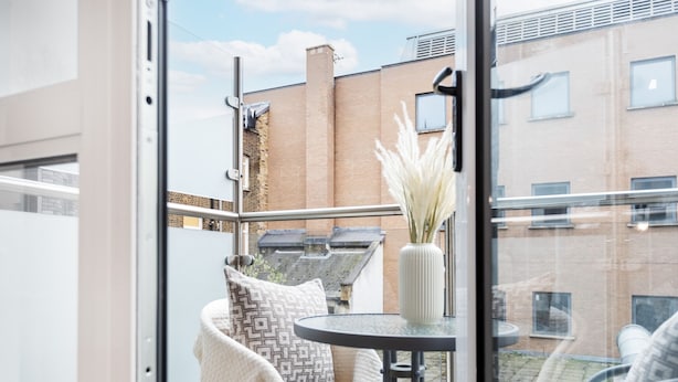 A balcony with a round table, a chair, and a vase with pampas grass. - Fitzrovia 1BR with Balcony by Soho (London)