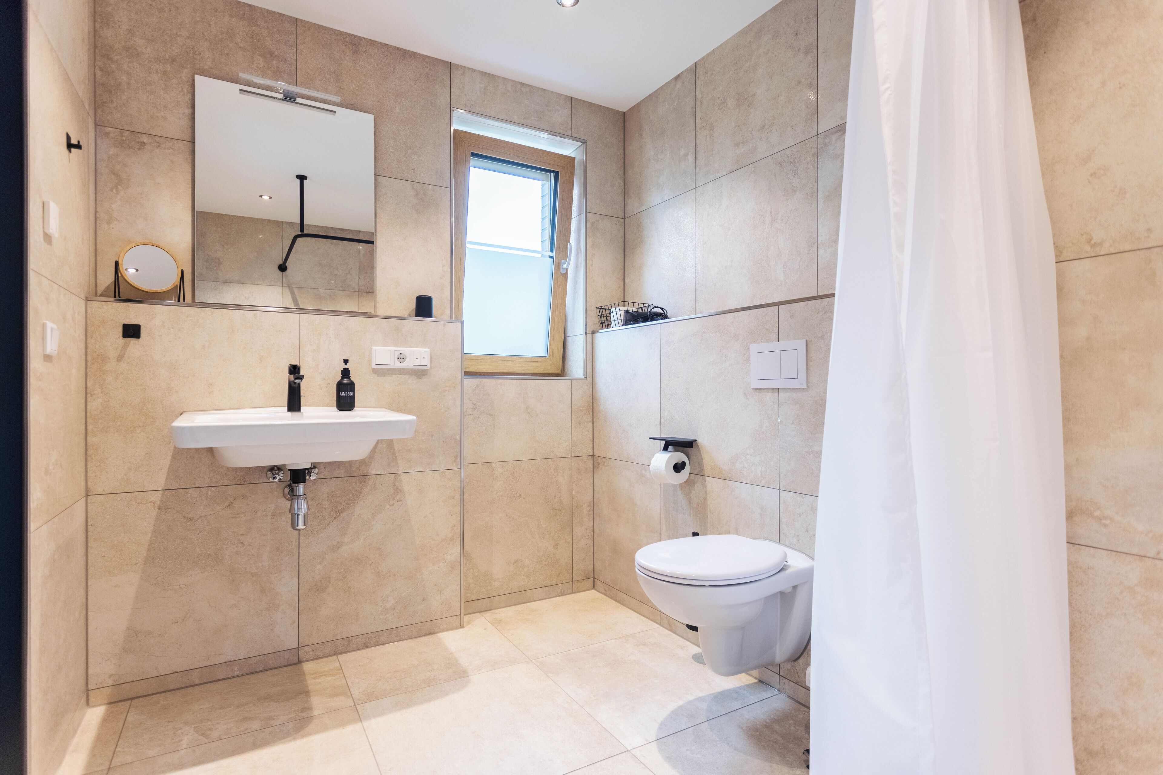 A modern bathroom with a sink, mirror, toilet, and a window.