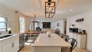 Une cuisine moderne dotée d’un îlot central, de meubles blancs et d’un coin repas avec des chaises.