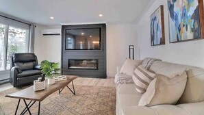 Un salon moderne avec un canapé en cuir noir, un canapé beige, une table basse en bois et une cheminée.
