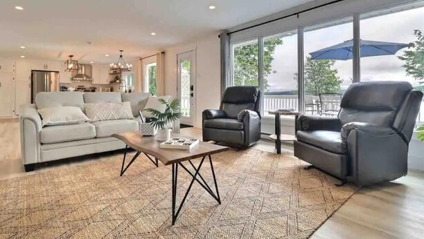 Un salon spacieux comprenant un canapé, deux fauteuils, une table basse et une grande fenêtre donnant sur l’extérieur.