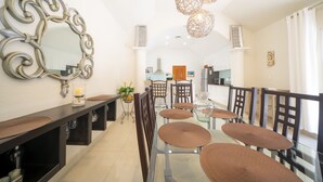A modern dining area with a glass table, brown woven placemats, and dark wooden chairs. A large ornate mirror and decorative lighting are visible. - Villa Perla 15 At Playacar phase ll NAS (Playa del Carmen)
