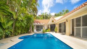 A swimming pool with a tiled edge, surrounded by lush greenery and a house with a tiled roof and large windows. - Villa Perla 15 At Playacar phase ll NAS (Playa del Carmen)