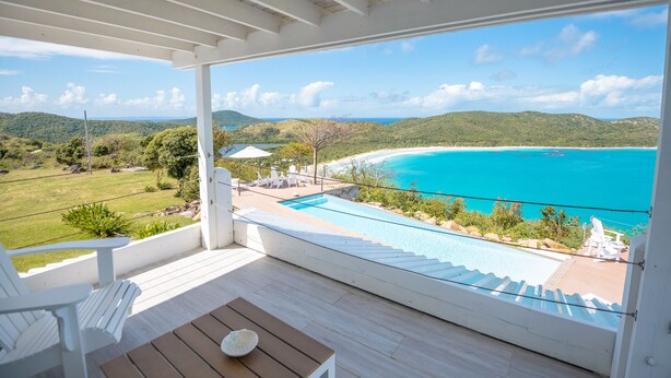 En balkon med udsigt over en turkis strand og en swimmingpool.