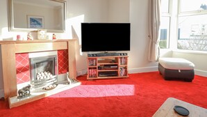 A living room with a fireplace, a television, a bookshelf, and a window with curtains. - Eden Retreat (Par)