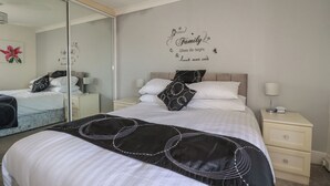 A neatly arranged bedroom with a large bed, two bedside tables, a mirror, and a wall decal. - Eden Retreat (Par)