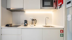 Une petite cuisine équipée d’un four à micro-ondes, d’une machine à café, d’une bouilloire et d’un évier.