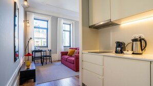 Une cuisine compacte équipée d’une machine à café et d’une bouilloire de marque Bosch, un coin repas avec une table et des chaises, et un canapé rose.