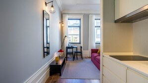 Un couloir étroit mène à un espace repas comprenant une table et des chaises, un canapé rouge et un coin cuisine avec une cuisinière.