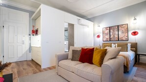 A modern bedroom with a beige sofa, a bed with multiple pillows, a large wall art piece, and a visible bathroom. - Sta. Catarina 632 - 2T by LovelyStay (Porto)