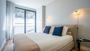A bedroom with a large bed, a nightstand, a lamp, and a view of the outdoors through a sliding door. - Sta. Catarina 632 - 3 by LovelyStay (Porto)