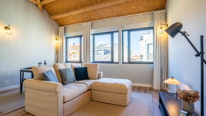 A cozy living room with a beige sectional sofa, a small side table, and a floor lamp. Large windows offer a view of the cityscape. - Sta. Catarina 632 - 3 by LovelyStay (Porto)