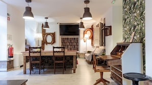 A cozy, well-lit room with a wooden dining table, chairs, a bookshelf, and a television.
