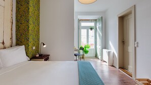 A bedroom with a large bed, a nightstand with a lamp, a chair, and a view of the outside through a door.